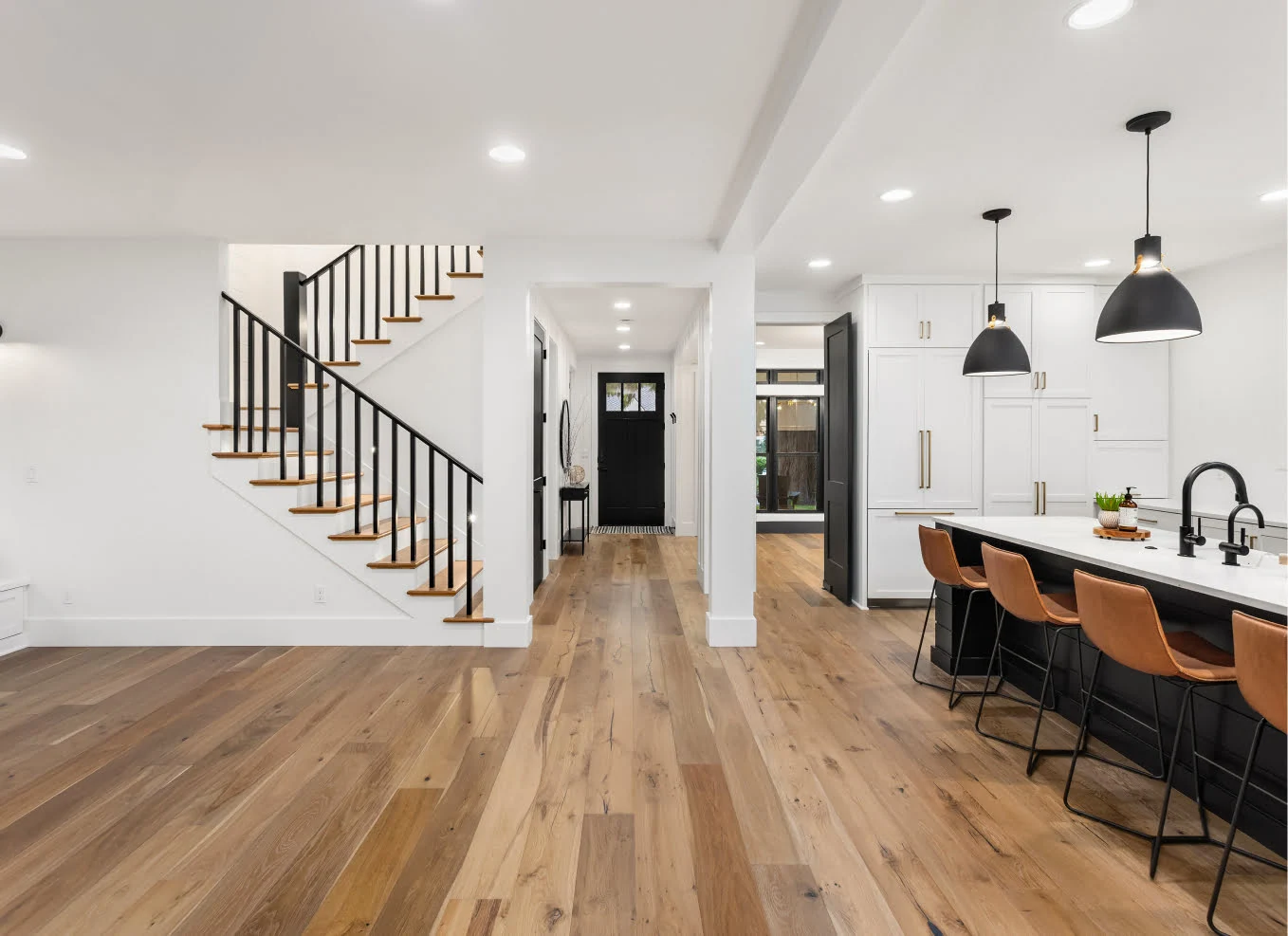 Modern open-concept kitchen and dining area with a large island, pendant lights, wooden flooring, and a staircase leading to the upper level.